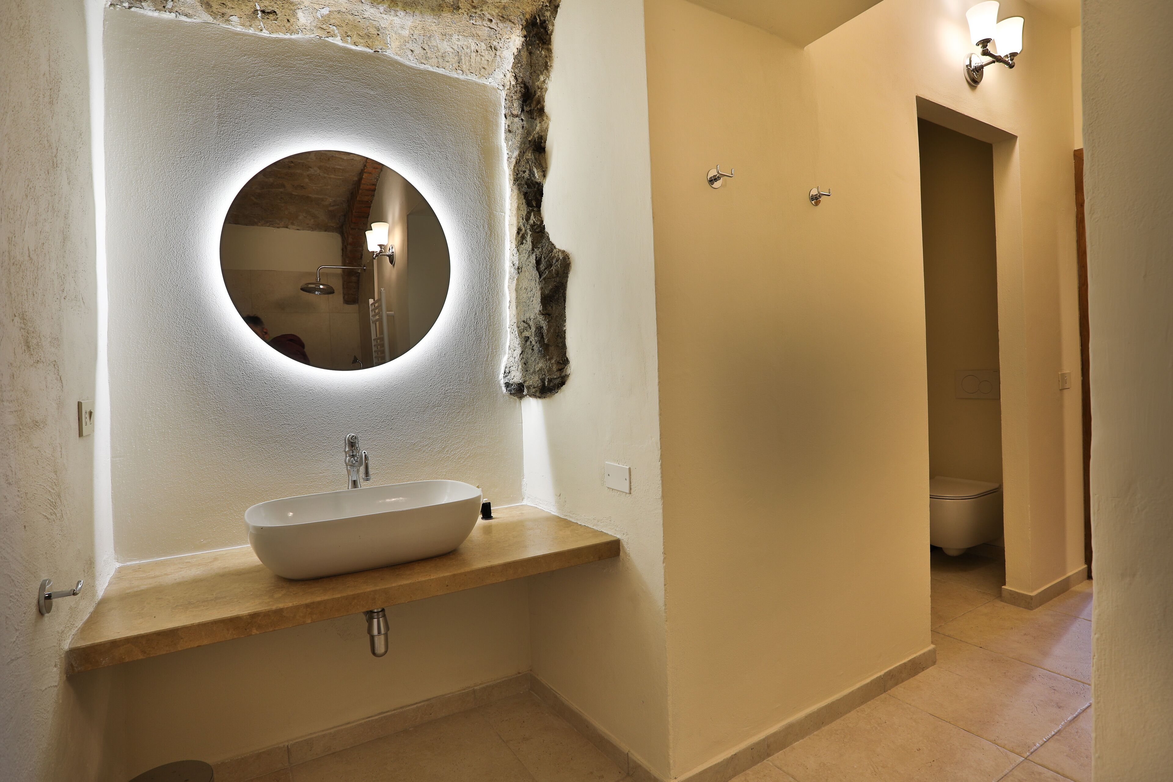 A bathroom with a round mirror, a vessel sink, and a light fixture above the mirror.