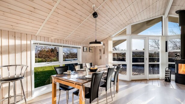 Un vaste espace dédié à la salle à manger, avec une table et des chaises en bois, de grandes fenêtres et une vue sur l’extérieur.