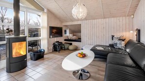 Un salon moderne avec un poêle à bois, une grande fenêtre, un canapé et une table à manger.