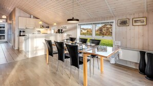 Une cuisine spacieuse avec des meubles en bois, un coin repas comprenant une table et des chaises, et de grandes fenêtres offrant une vue sur l’extérieur.