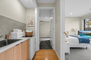 Een moderne hotelkamer met een bed, een badkamer met een wastafel en handdoeken, en een gang die naar een andere kamer leidt.