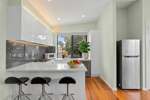 A modern kitchen with a central island, bar stools, a refrigerator, and a window with a view. - Luxury 3BR Maidstone Townhouse | Near Highpoint & Melbourne CBD (Maidstone)