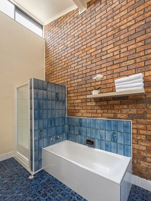 A bathroom with a bathtub, a shower enclosure, and a brick wall. - Jalynca - Waterfront Escape (Noosa)