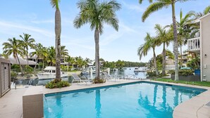 A swimming pool surrounded by palm trees and a marina with boats.