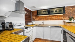 A compact kitchen with a brick wall backsplash, a stainless steel range hood, a built-in oven, and a double sink.