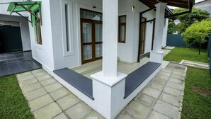 A covered outdoor area with a tiled floor, white walls, and a green metal structure.