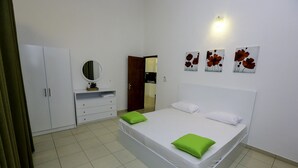A bedroom with a bed, a dresser, a mirror, and a door leading to a kitchen.