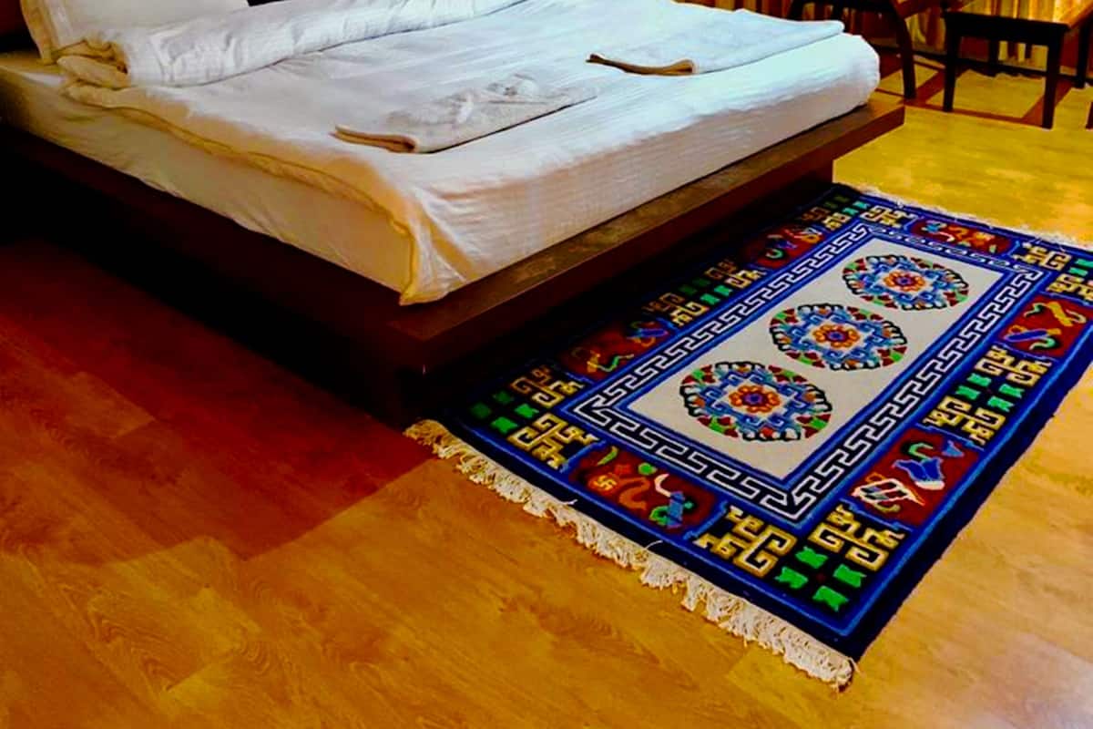 Ett hotellrum med en stor säng, en sänggavel i trä, ett litet bord och en färgglad matta.