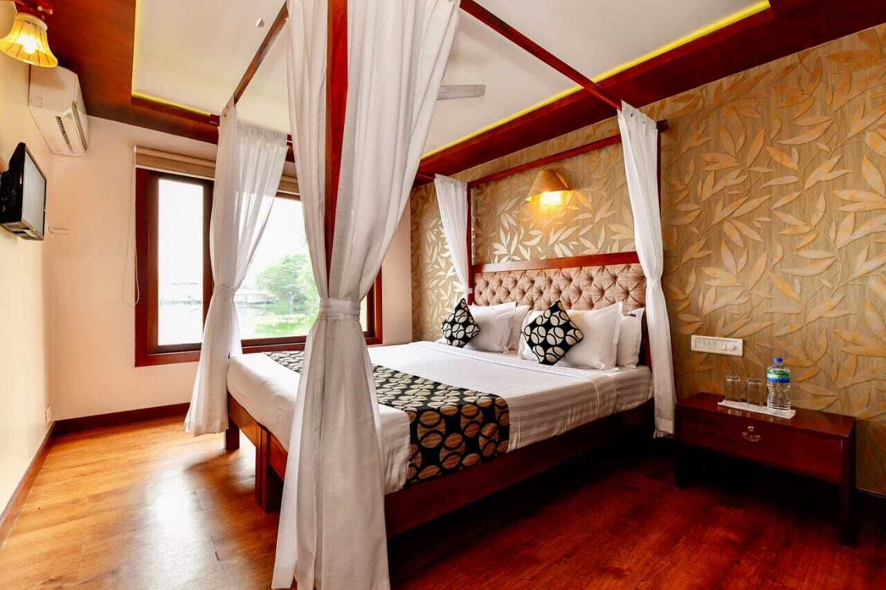 A bedroom with a four-poster bed, a wooden floor, a nightstand with a water bottle, and a wall with a leaf pattern.