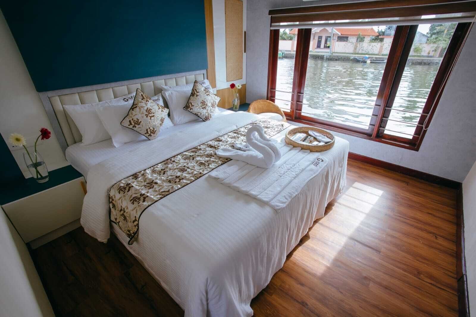 A bedroom with a bed, pillows, a bedside table with a vase, and a window with a view of water.