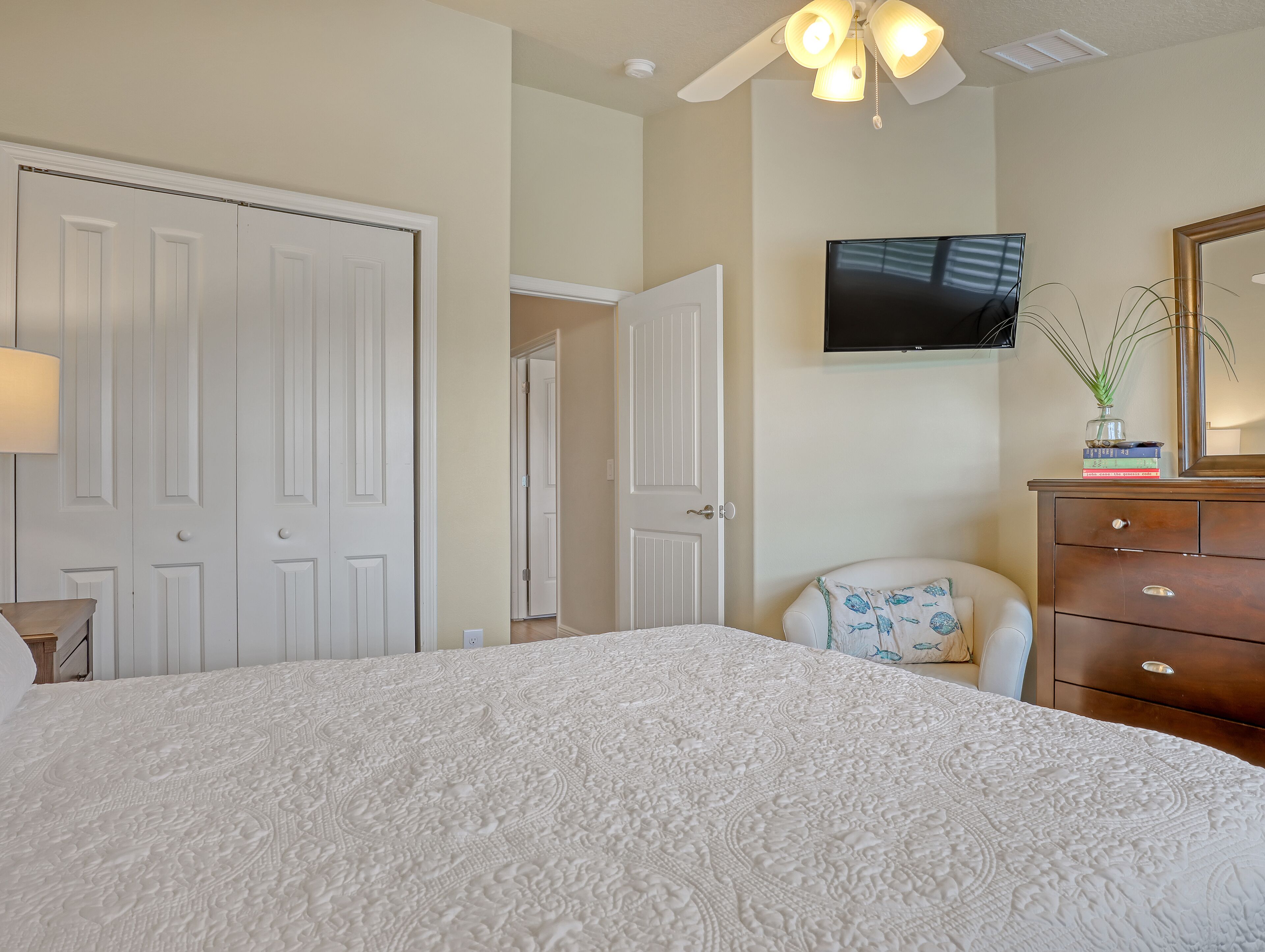 A bedroom with a large bed, a dresser, a chair, a television, and a ceiling fan.