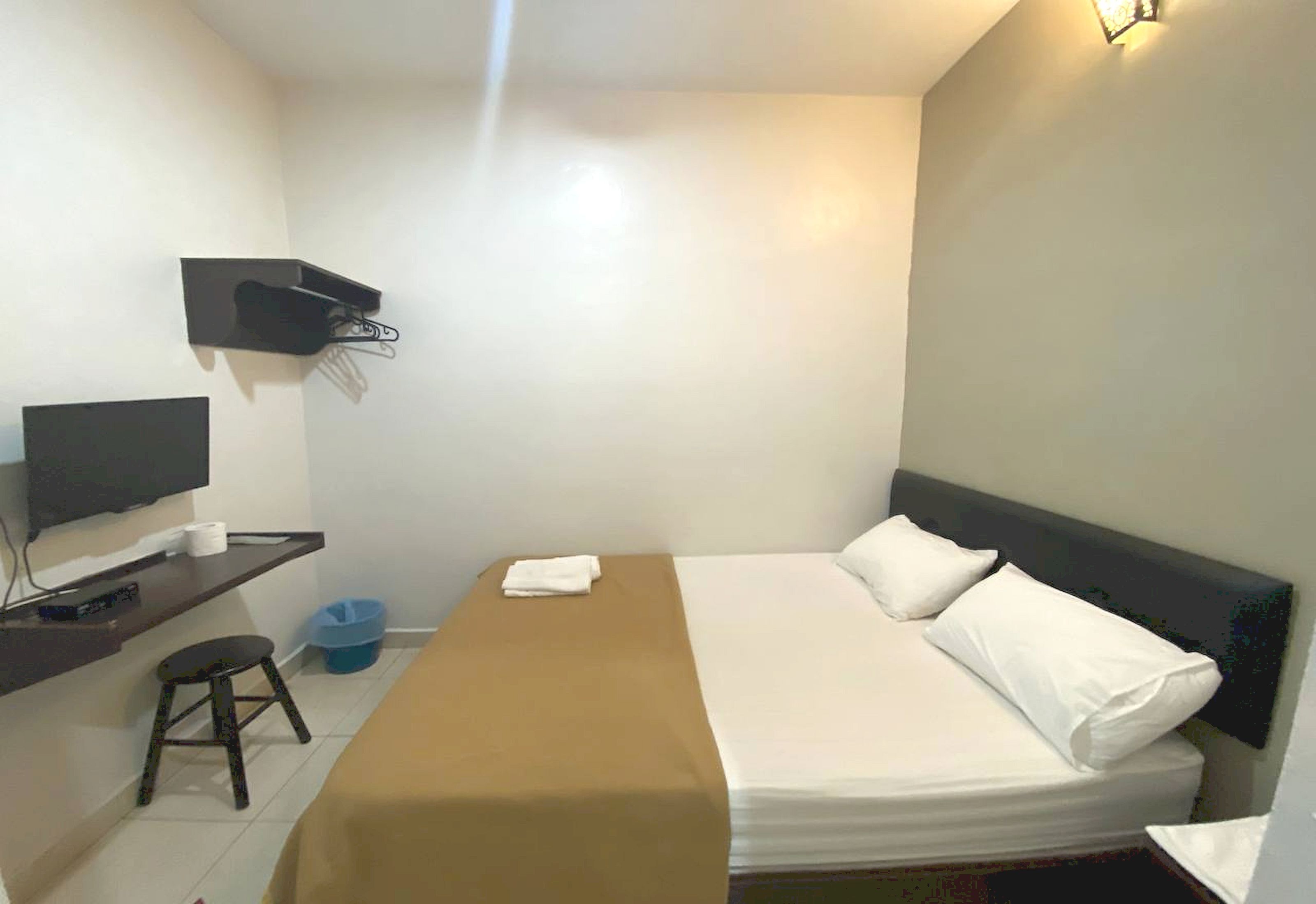 A small, clean room with a bed, a TV, a desk, and a wall-mounted shelf.