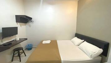 A small, clean room with a bed, a TV, a desk, and a wall-mounted shelf.