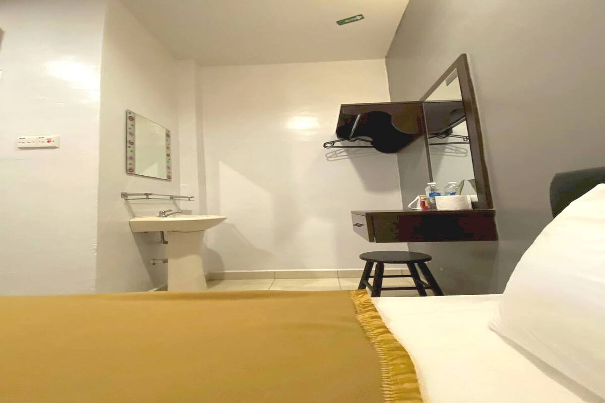 A hotel room with a bed, a bedside table, a mirror, a sink, and a small stool.