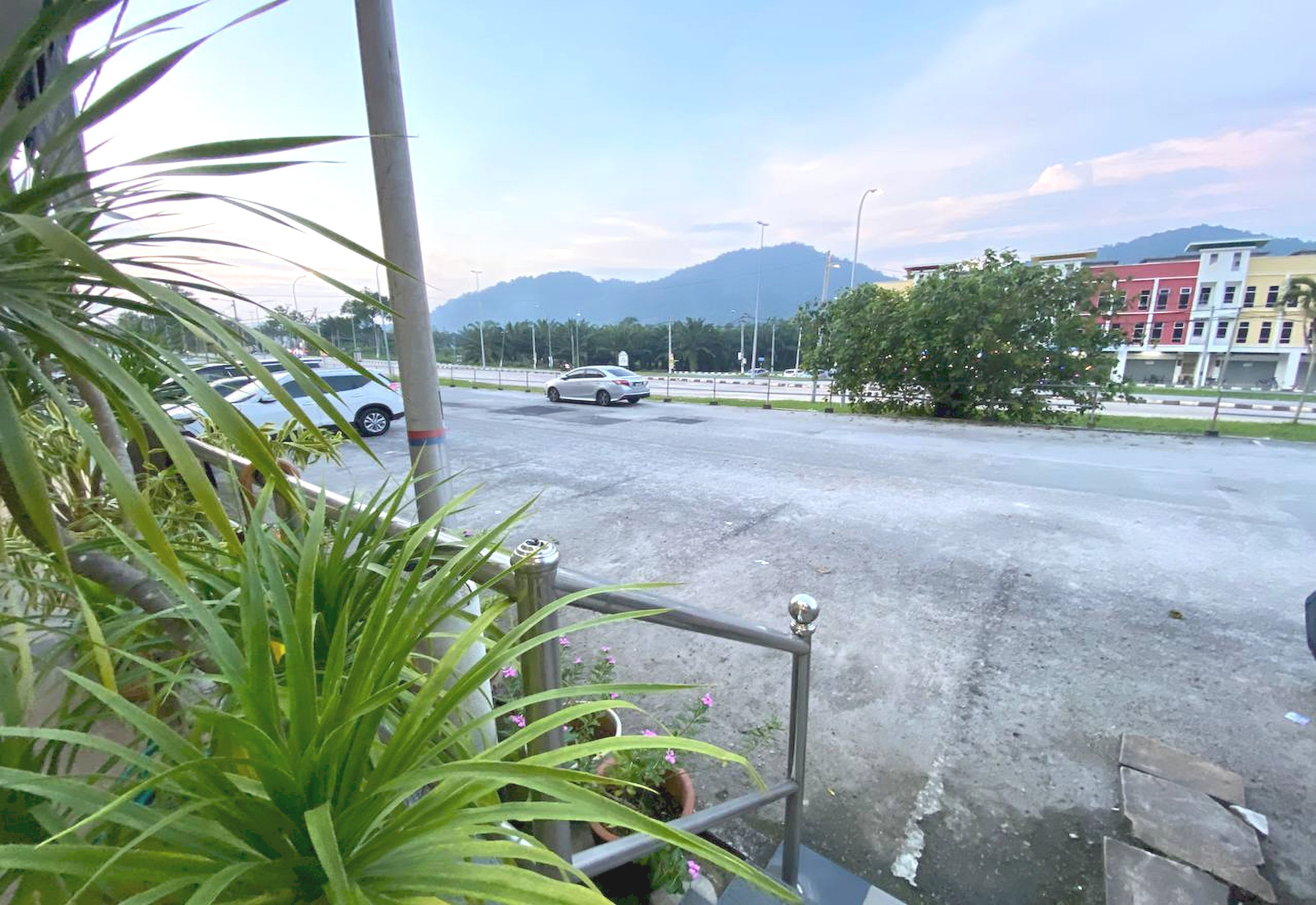 Un estacionamiento con un coche blanco, plantas en macetas y una vista de edificios y montañas al fondo.
