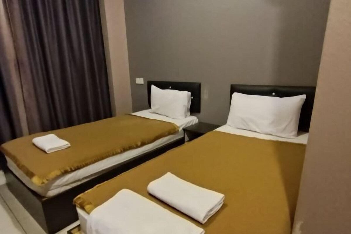 A hotel room with two single beds, each with a brown bedspread and white pillows.
