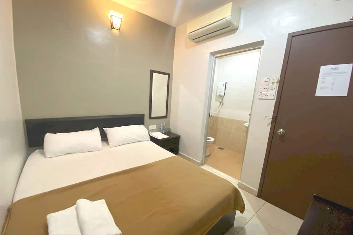 A hotel room with a bed, bedside table, lamp, and an air conditioning unit.