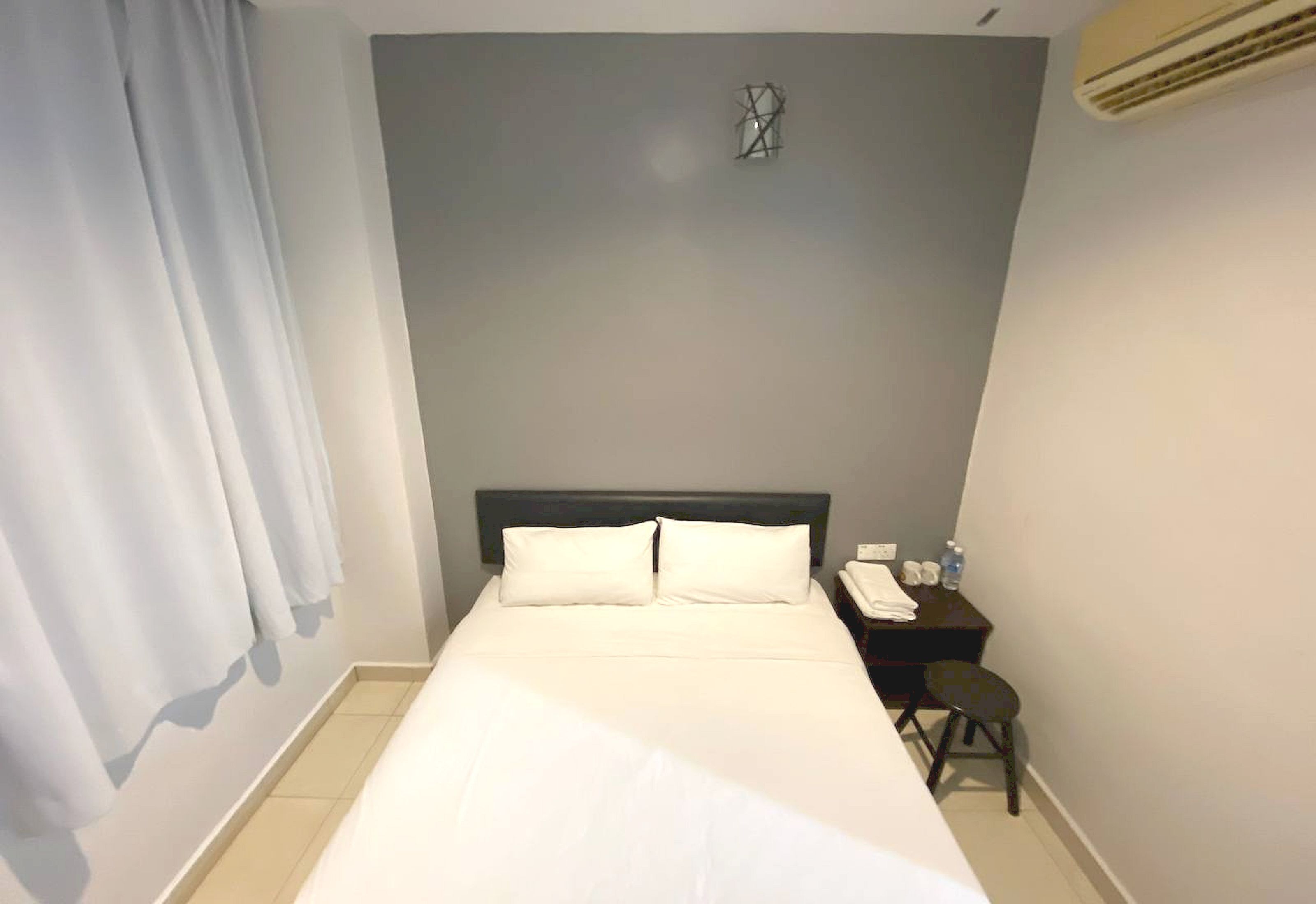 A hotel room with a bed, a nightstand, a chair, a desk, and a wall-mounted air conditioner.