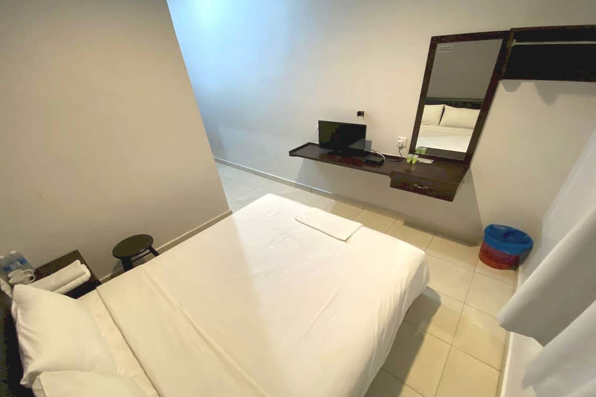 A hotel room with a bed, a small desk with a computer, a mirror, and a trash bin.
