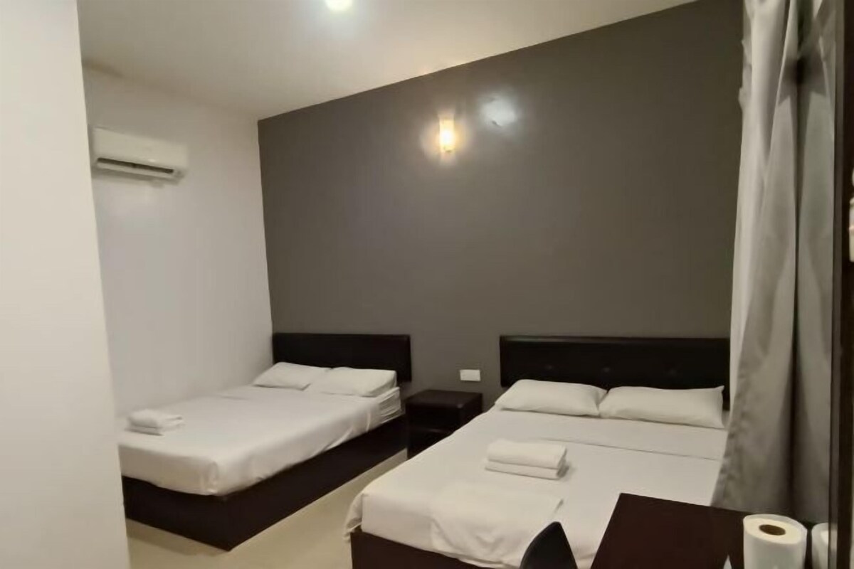 A hotel room with two beds, a desk, and an air conditioning unit.