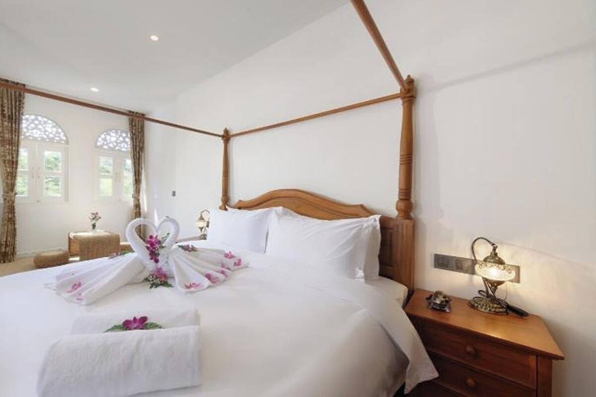 Ein Himmelbett mit Schwaneinrichtung, ein Nachttisch mit Lampe und ein Fenster mit Vorhängen.