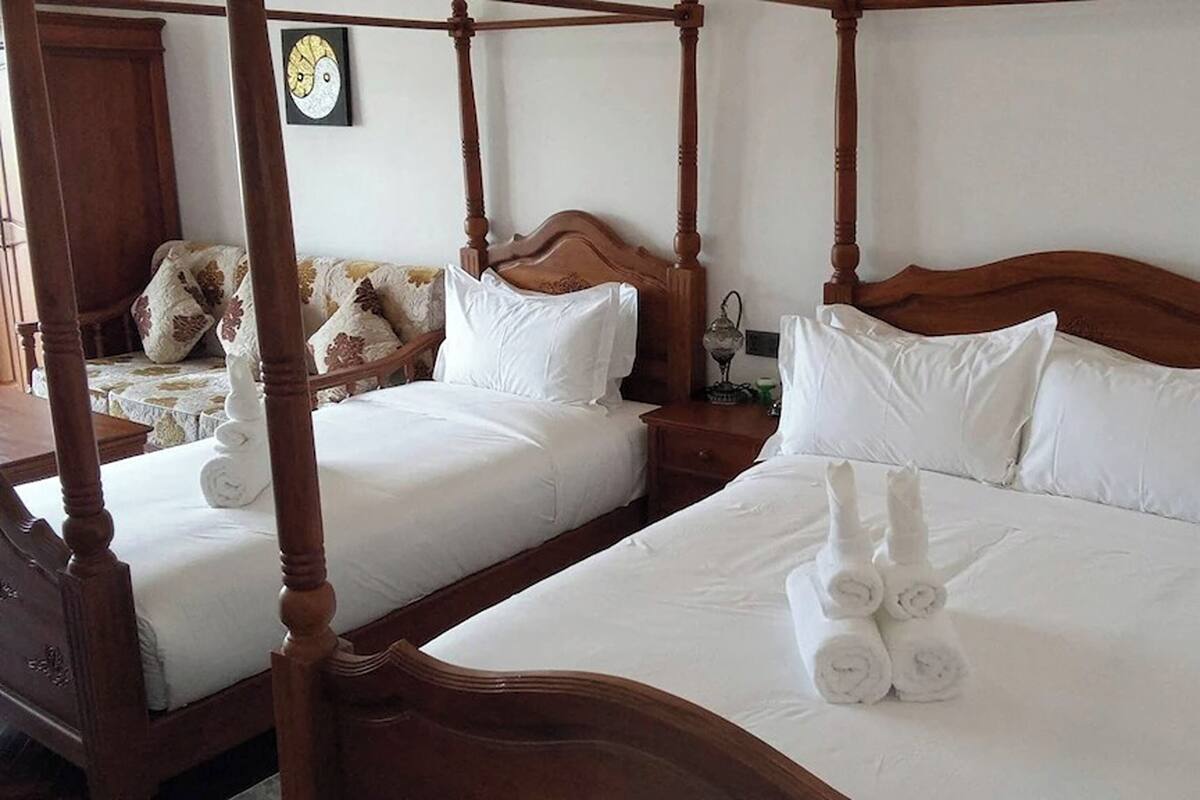 Ein Bett mit Baldachin, ausgestattet mit weißen Leinen und gerollten Handtüchern, ein Nachttisch aus Holz und eine Wanduhr.
