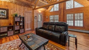 A log cabin interior with a leather sofa, wooden shelves, and large windows.