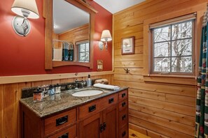 Un baño de cabaña de madera con un espejo grande, encimera de granito y armarios de madera.