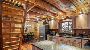 A rustic kitchen with wooden beams, a granite countertop, and a dining area with a table and chairs.