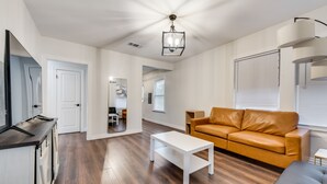 Een ruime woonkamer met een houten vloer, een witte salontafel, een leren bank en een moderne kroonluchter.