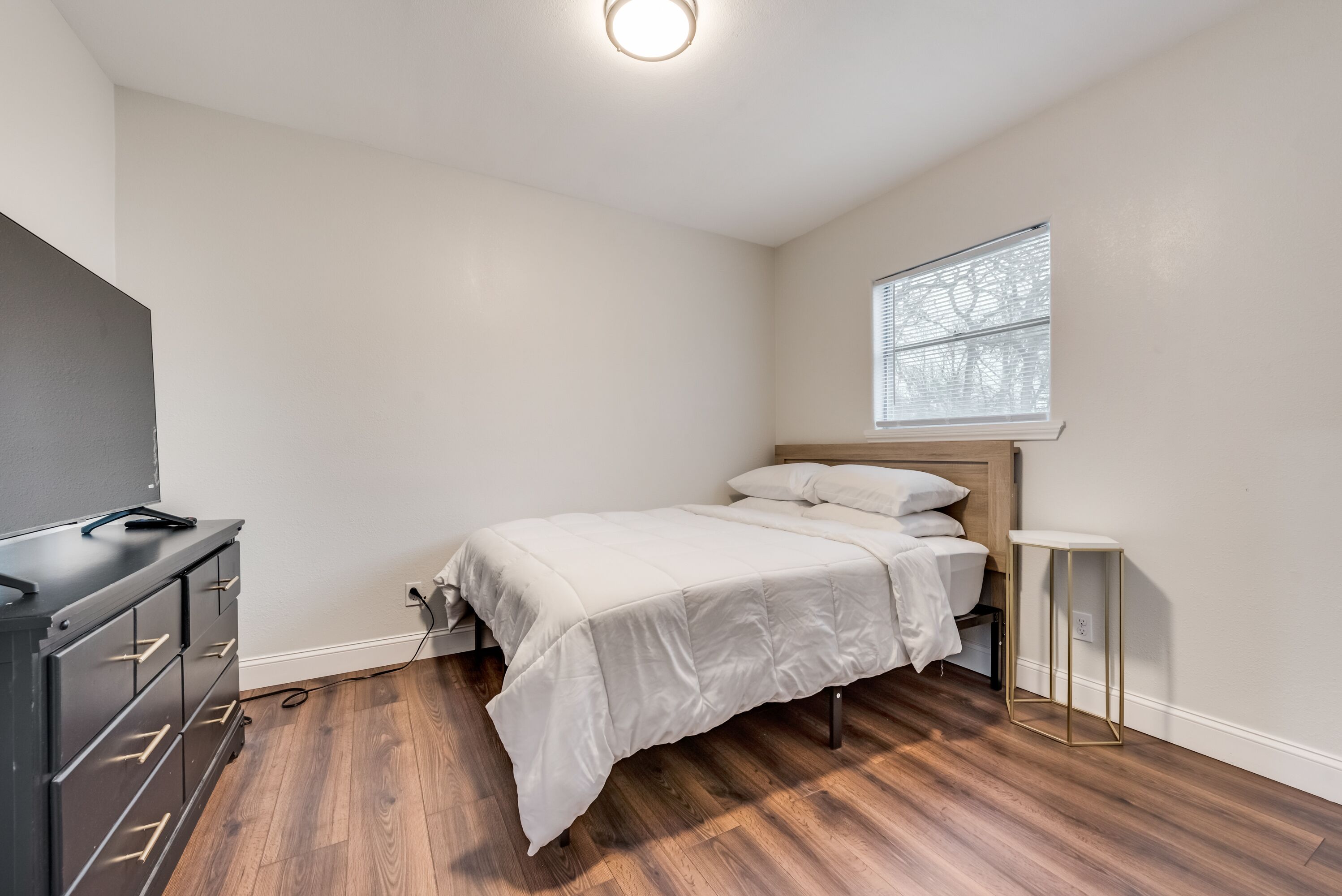 Un dormitorio con cama, cómoda, mesita de noche y ventana con persianas.