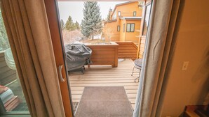 Une terrasse en bois avec un barbecue, un espace salon extérieur couvert et une vue sur une maison en bois en arrière-plan.