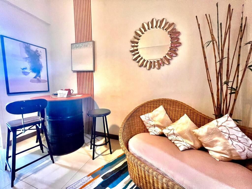 Une pièce comprenant un canapé en osier, deux chaises noires, une table ronde et un miroir décoratif accroché au mur.