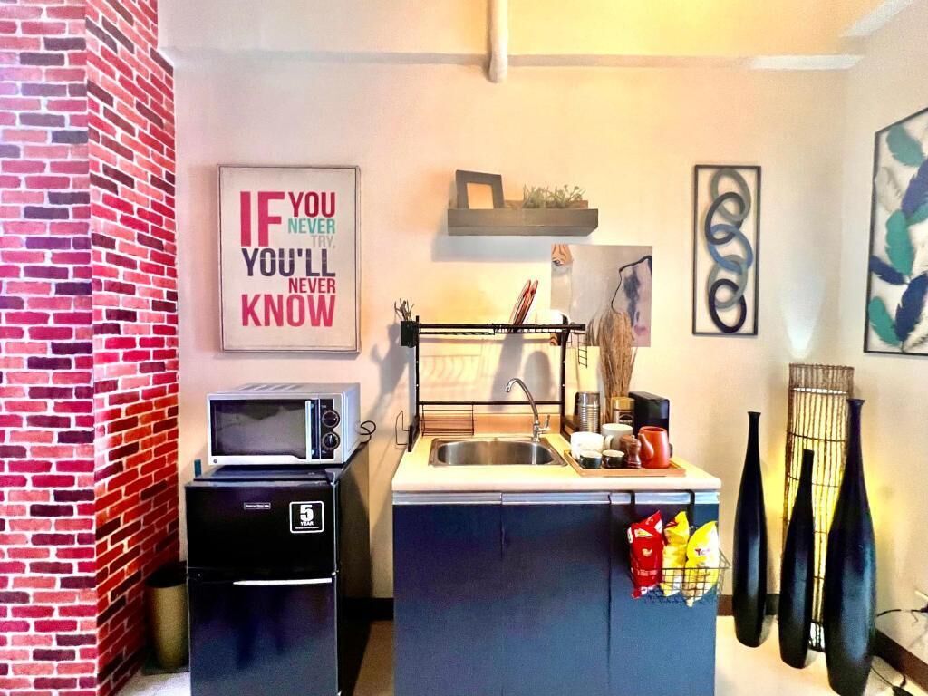 Eine kompakte Küche mit Mikrowelle, Kühlschrank und Spüle. An der Wand ist ein motivierendes Zitat zu sehen und über der Spüle befindet sich ein kleines Regal.