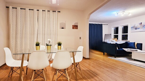 A modern living room with a dining area, featuring a glass table, white chairs, a blue sofa, and a small side table. - 3 Bedroom 10min Walk to the UofA/Hospital.   (Edmonton)
