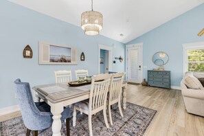 A dining area with a wooden table and chairs, a hanging light fixture, and a patterned rug.