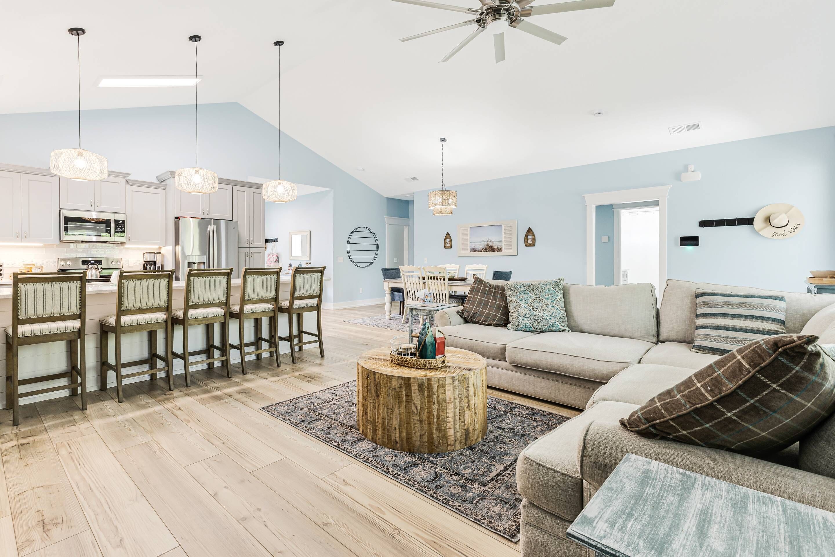 A spacious living room with a high ceiling, a dining area with wooden chairs, and a kitchen with modern appliances.