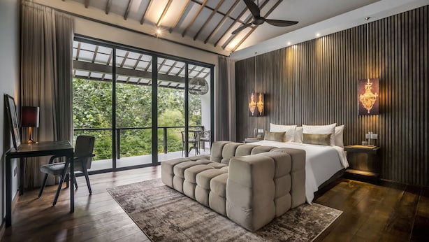 Un dormitorio moderno con una cama grande, zona de estar, escritorio y balcón con vistas a zonas verdes.