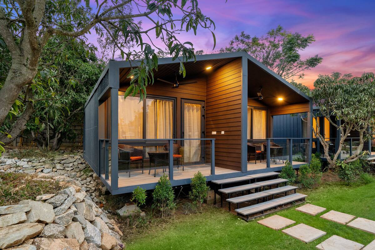 A modern cabin with a glass balcony, wooden deck, and a stone wall.