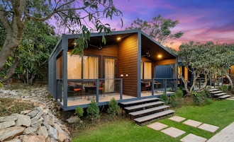 Uma cabana moderna com varanda de vidro, deck de madeira e parede de pedra.