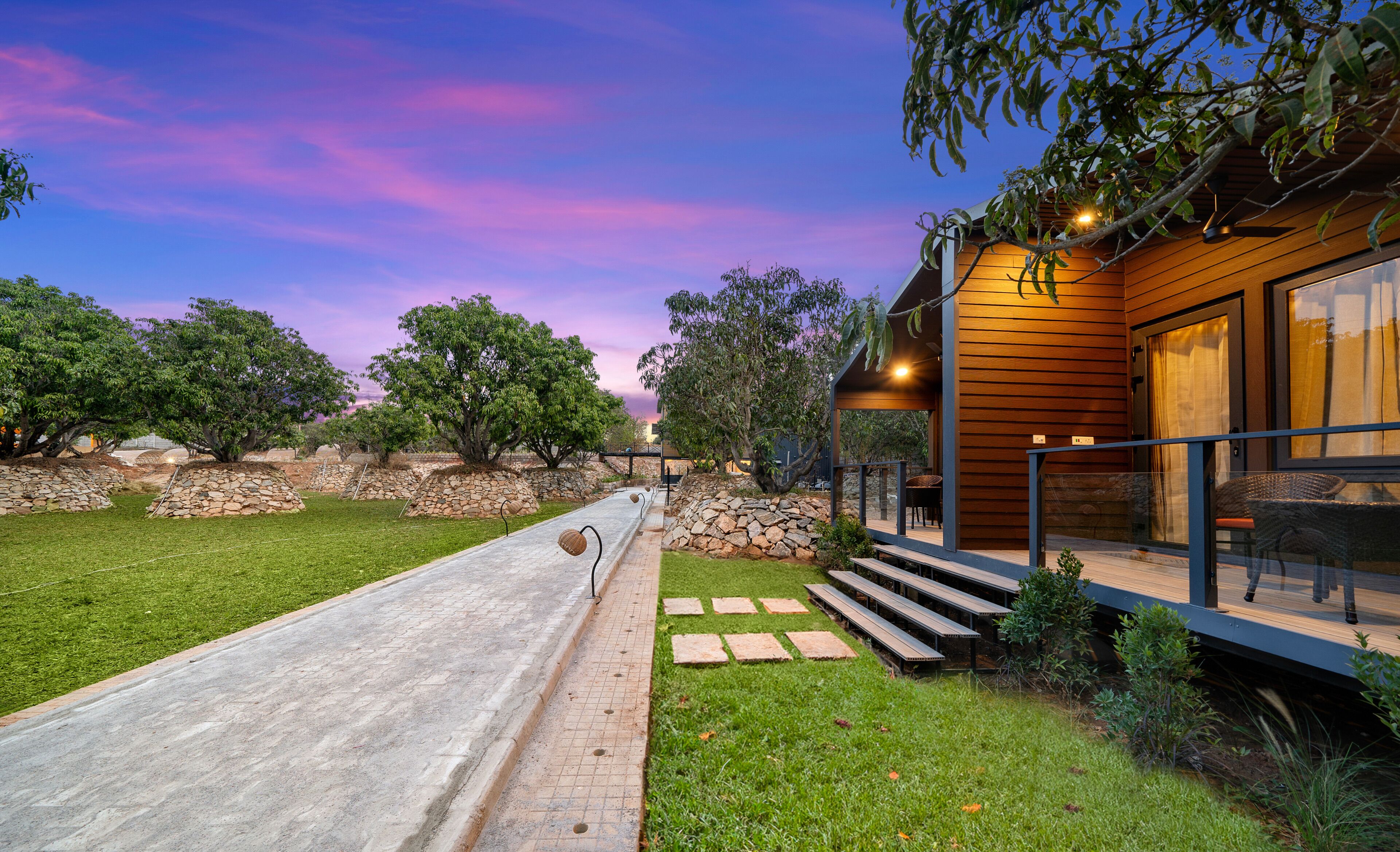 A modern house with a stone pathway leading to a wooden deck, surrounded by greenery and trees.