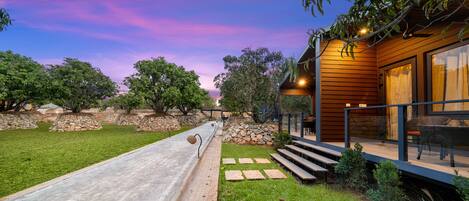 A modern house with a stone pathway leading to a wooden deck, surrounded by greenery and trees.
