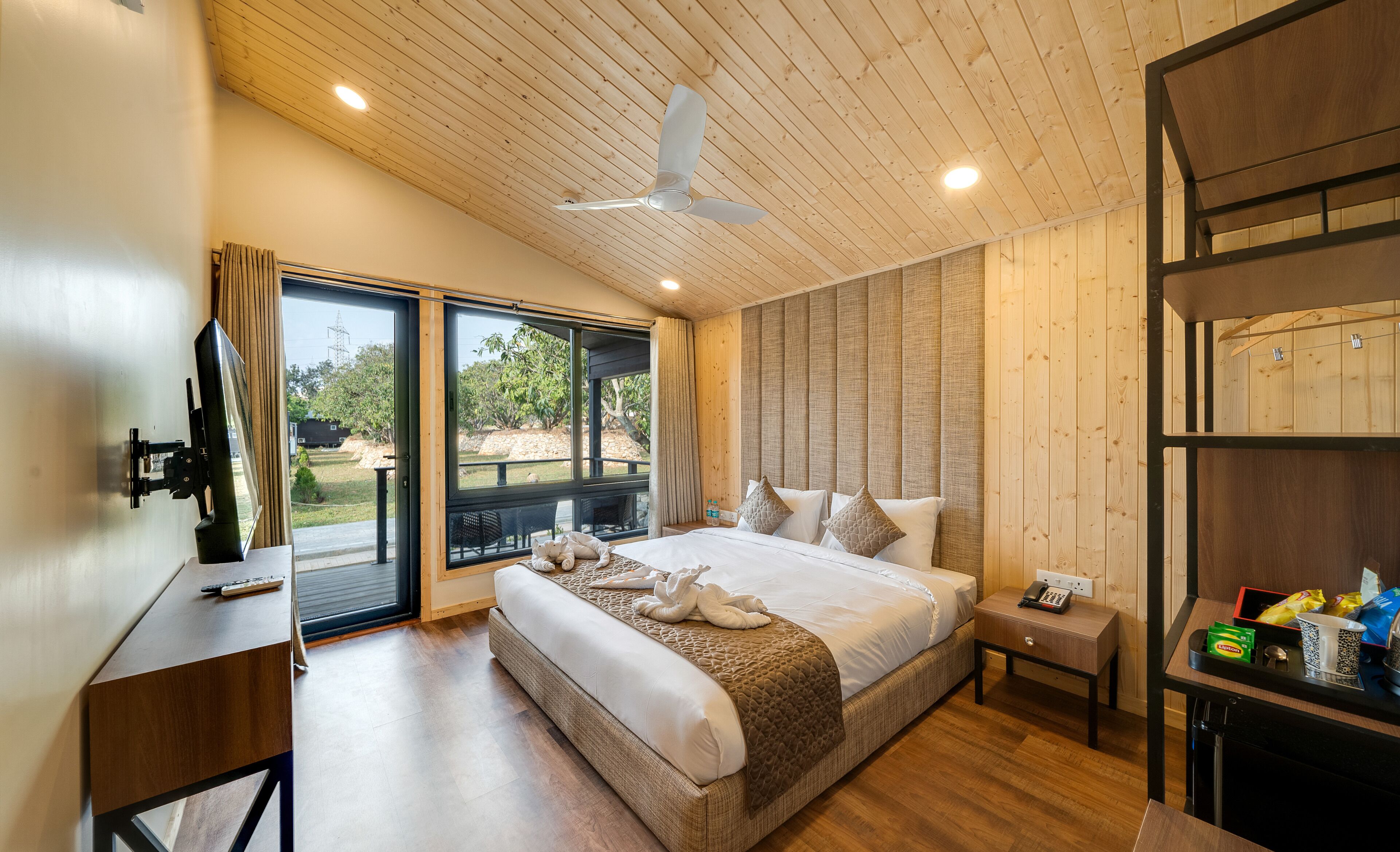 Un dormitorio amplio con una cama grande, ventilador de techo, piso de madera y vista al exterior por una puerta corrediza de vidrio.