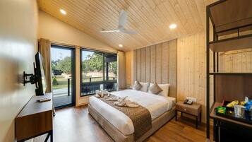 Un dormitorio amplio con una cama grande, ventilador de techo, piso de madera y vista al exterior por una puerta corrediza de vidrio.