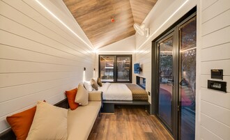 Quarto compacto com cama, um banco e porta de correr para área externa.