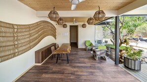 Un interno moderno con soffitto in legno, zona pranzo con un tavolo lungo e sedie, lampade pendenti in vimini e vista sull'esterno.