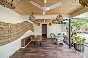Um interior moderno com teto de madeira, área de refeições com uma mesa comprida e cadeiras, luminárias suspensas de vime, e vista para o exterior.