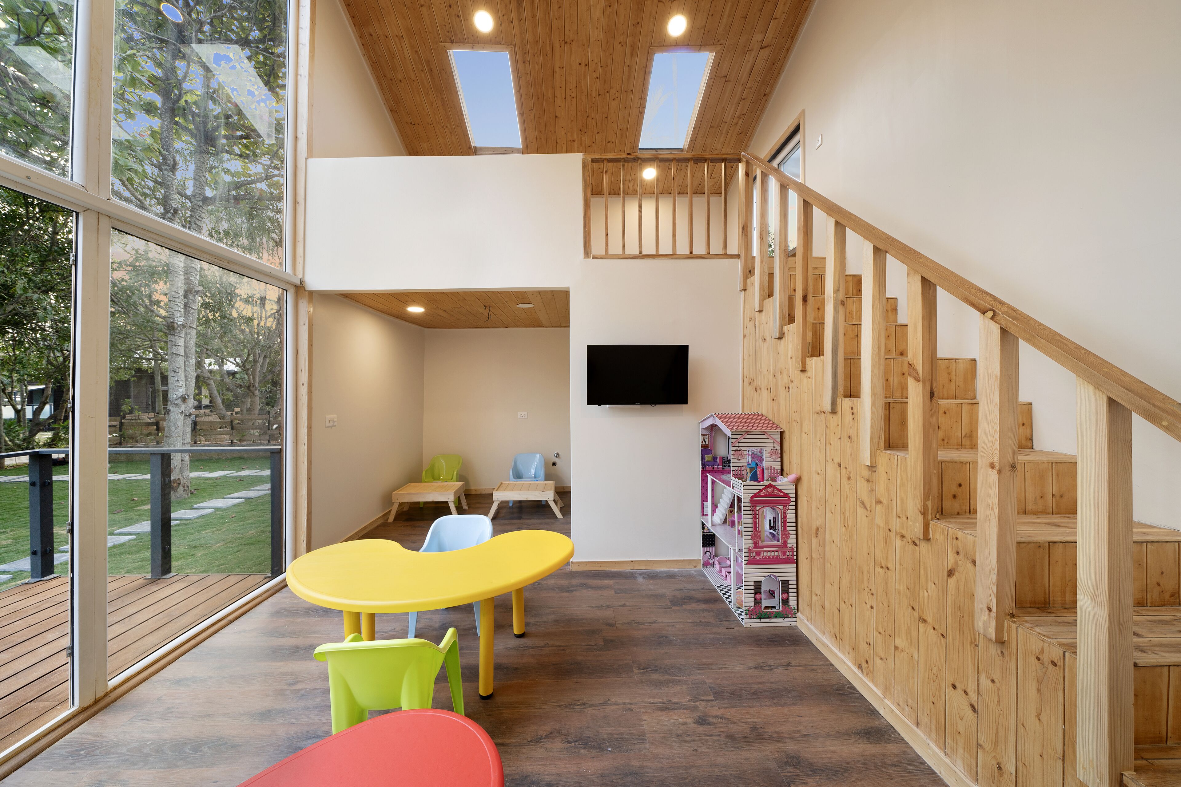 A spacious room with a wooden staircase, a large window, and a TV mounted on the wall.