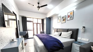 Un dormitorio moderno con cama, mesitas de noche, escritorio, silla, ventilador de techo y obras de arte en la pared.