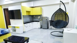 Una cocina moderna con armarios blancos y amarillos, un refrigerador de acero inoxidable y un sillón colgante.